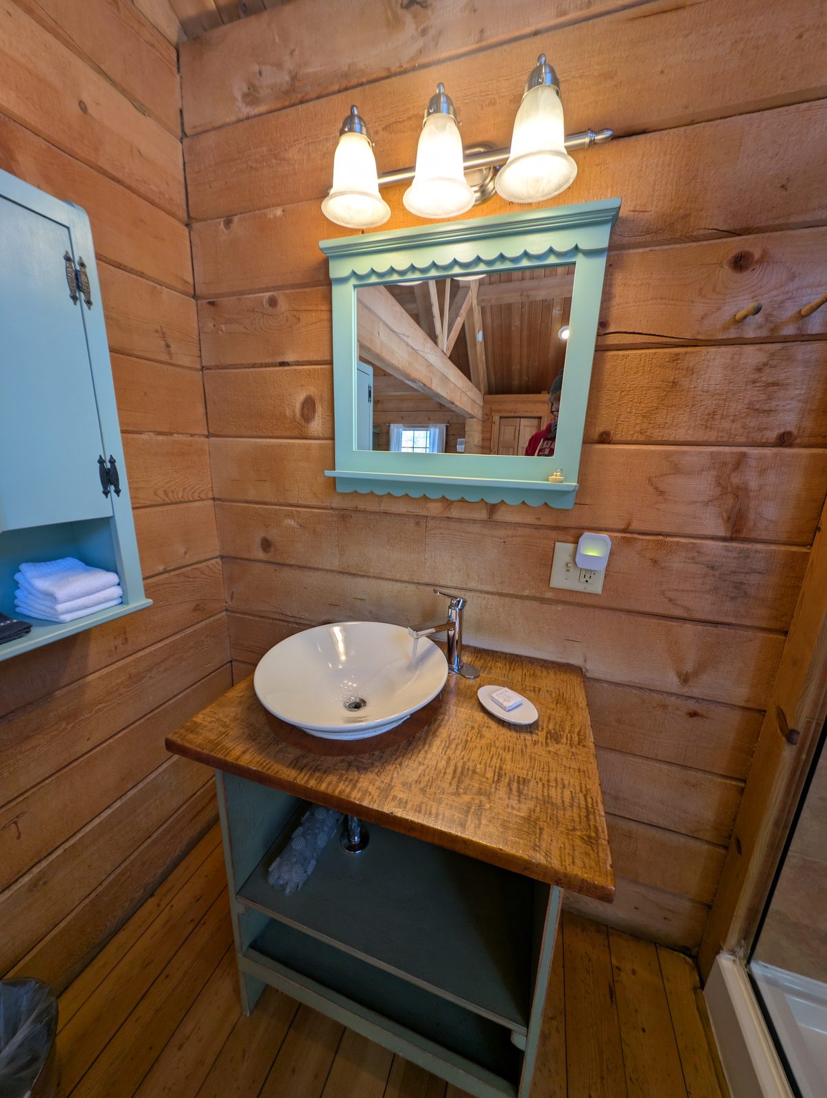 A vessel sink and painted mirror against a pine cabin wall